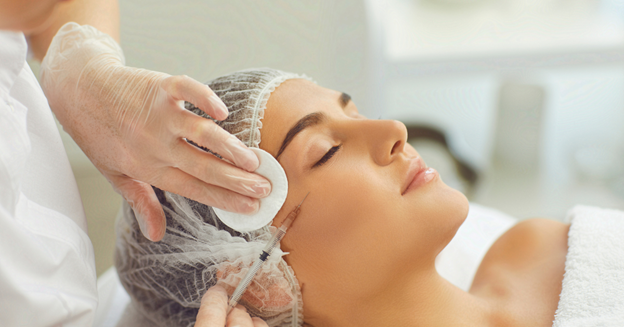 Woman relaxing with closed eyes while a provider in white gloves gently holds her face during treatment