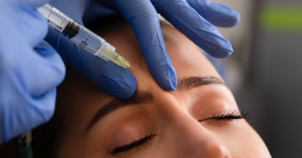 Provider in blue gloves injecting Dysport into a female’s forehead to smooth wrinkles