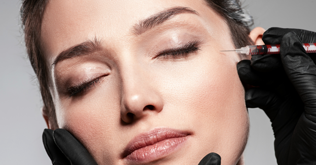 Close-up of a woman with closed eyes receiving a Botox injection near her temple