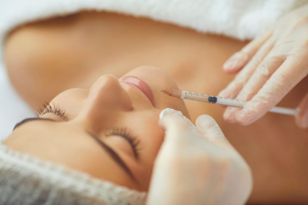 Cosmetologist injecting dermal lip filler into a woman's lips with a syringe