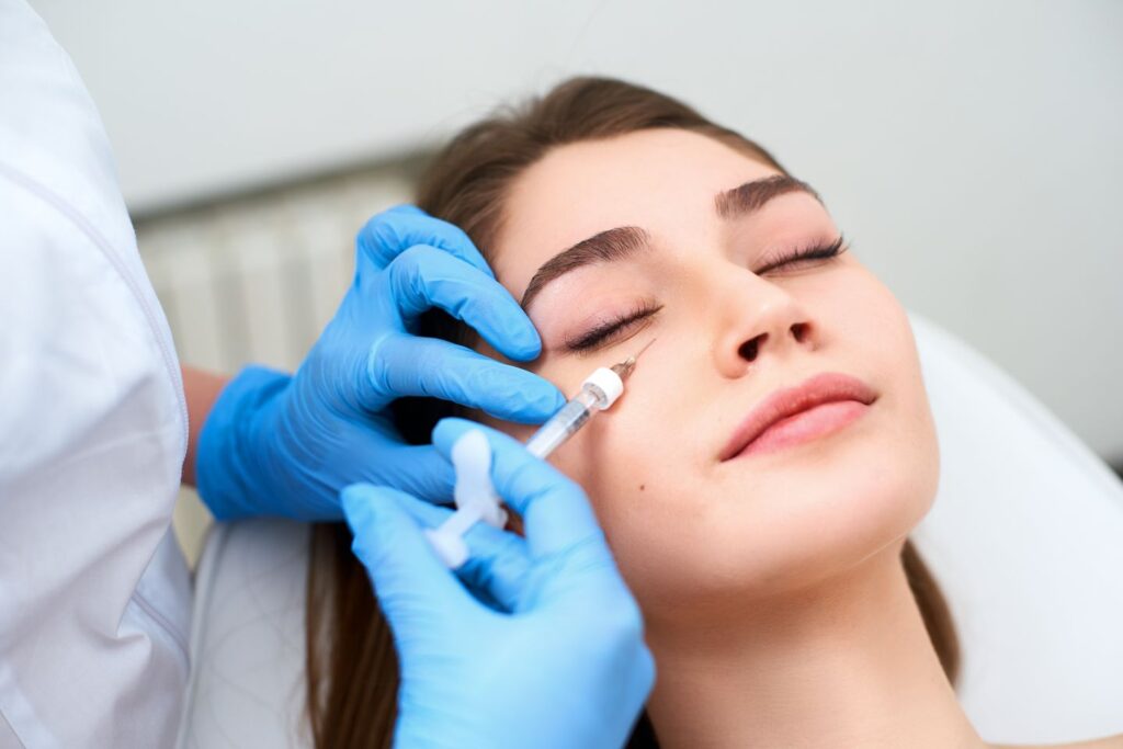 Clinician in gloves injecting under eye filler beneath a woman's eye