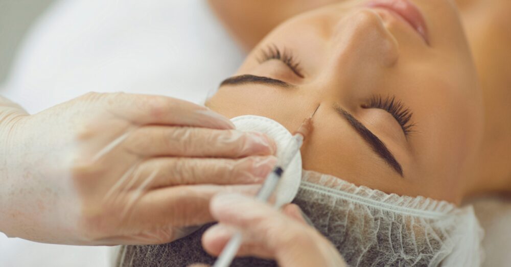 A gloved provider administering Botox injections into a woman’s forehead