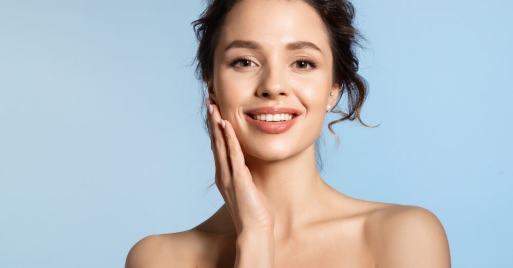 Woman touching her cheek while smiling against a blue background