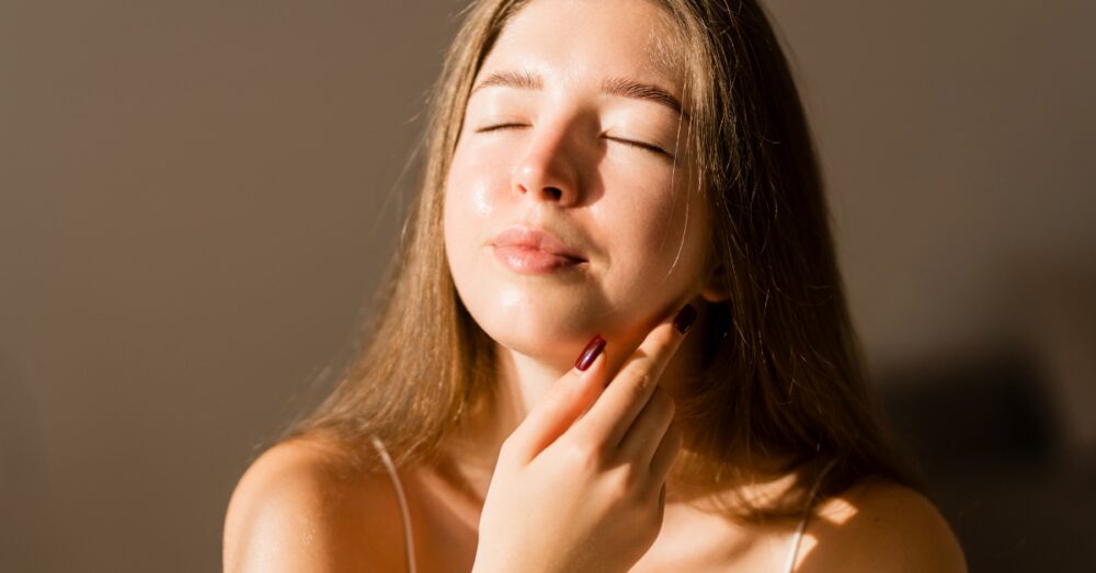 Woman gently touching her face while examining her skin with a calm expression