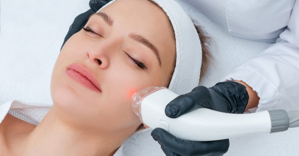Provider performing a laser skin treatment on a woman's face using a handheld device in a clinical setting