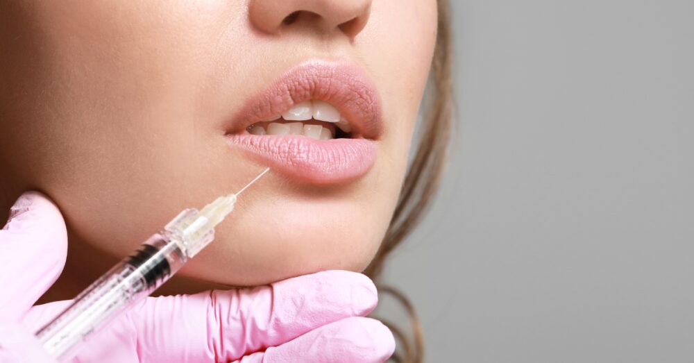 Close-up of a lip filler injection being administered near the mouth area using a fine needle while wearing pink medical gloves
